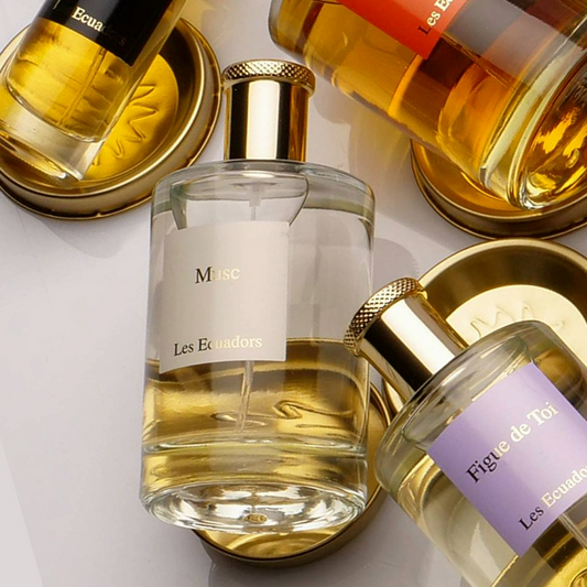 verschillende liggende parfumflessen op ronde goudkleurige schijven de middelste heeft de tekst Musc Les Ecuadors