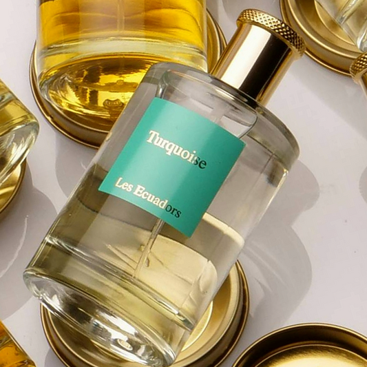 liggende parfumflessen op metalen goudkleurige schijven. de middelste fles heeft een blauw/groen label met de gouden tekst |Turquoise Les Ecuadors