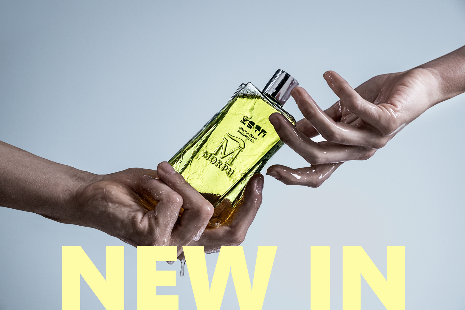 Twee natte handen houden een fles Morph Zeta douchegel vast met druppelend water – krachtige productfoto van nieuwe lancering bij Studio Aromatic, gelabeld met 'NEW IN'.